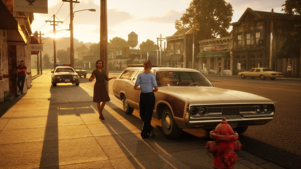 Officer talking with a civilian beside a parked car on a Winston Springs street at sunset